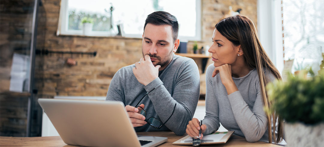 Pareja joven pensativa mirando portátil